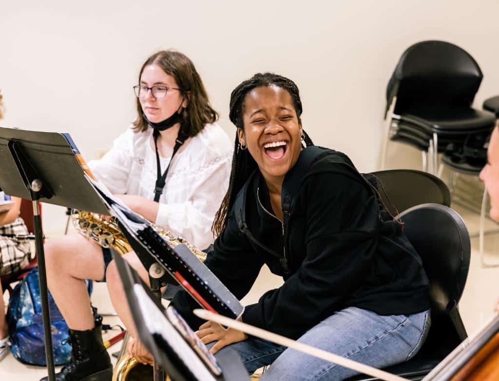 Summer music camp students laugh while sitting in front of music stands