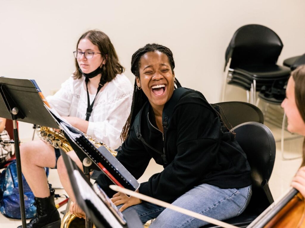 Summer music camp students laugh while sitting in front of music stands