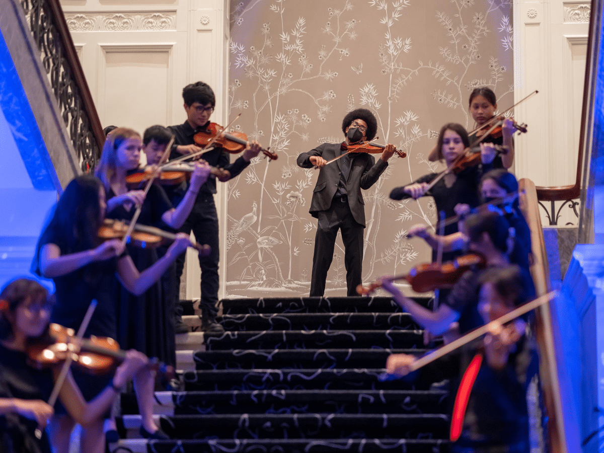 Violinists in formal attire play while standing on a staircase.