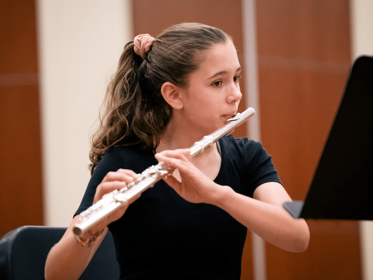 A student plays flute, looking at her music stand.