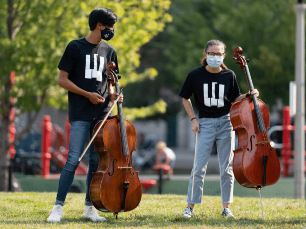 Two students walk outside holding cellos