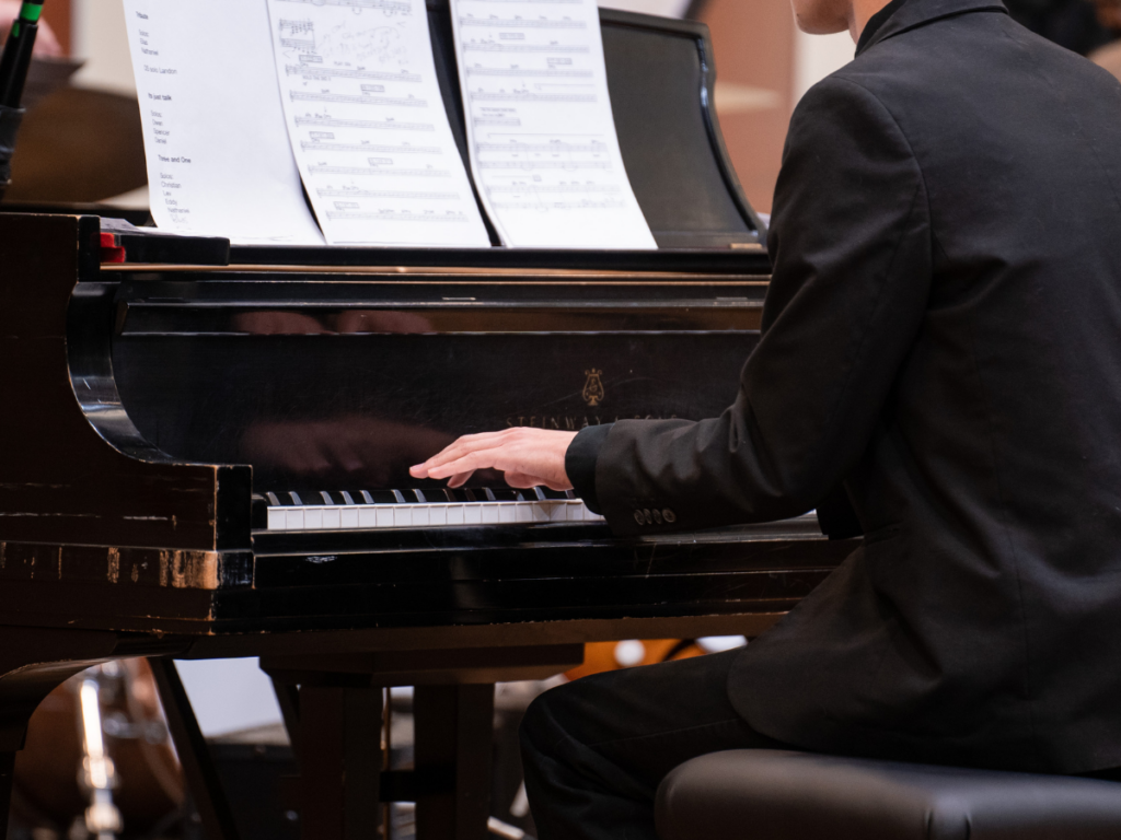 A photo showing a student in a suit playing a grand piano.