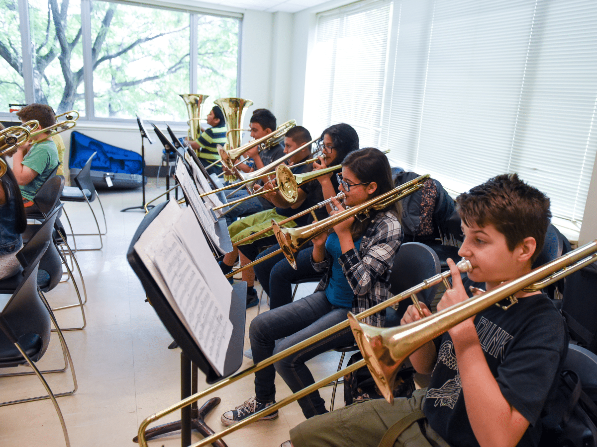 A line of young students, seated and playing trombones.