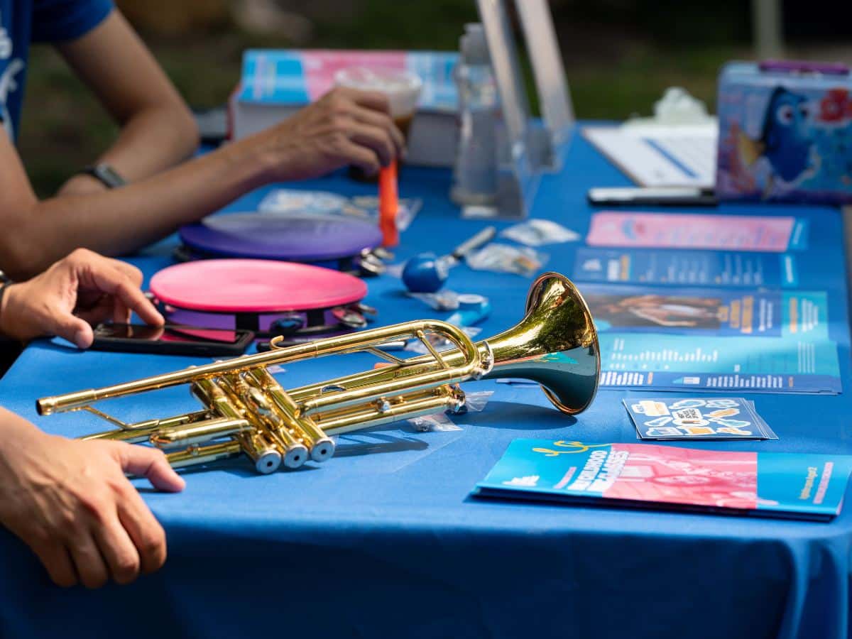 A close up of a table with a blue tablecloth at an open house. On the table is a trumpet, a tambourine, and flyers.