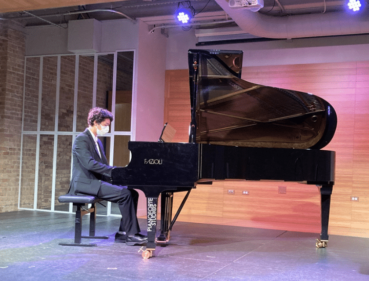 A student wearing a mask plays piano onstage at PianoForte Recital Hall.