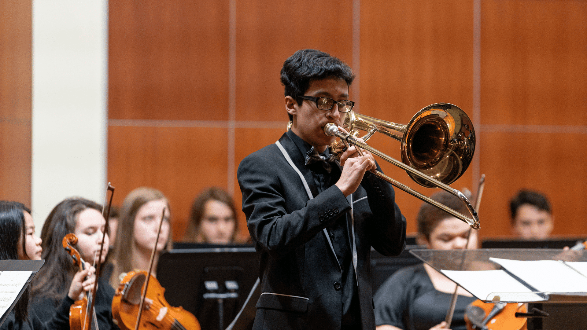 A trombone soloist stands in front of the orchestra at a Conservatory concert.