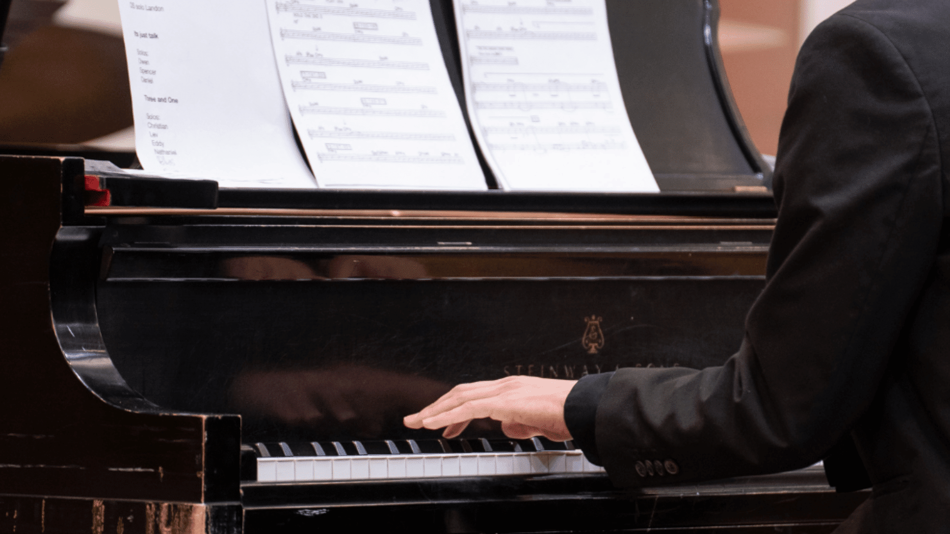A photo showing a student in a suit playing a grand piano.