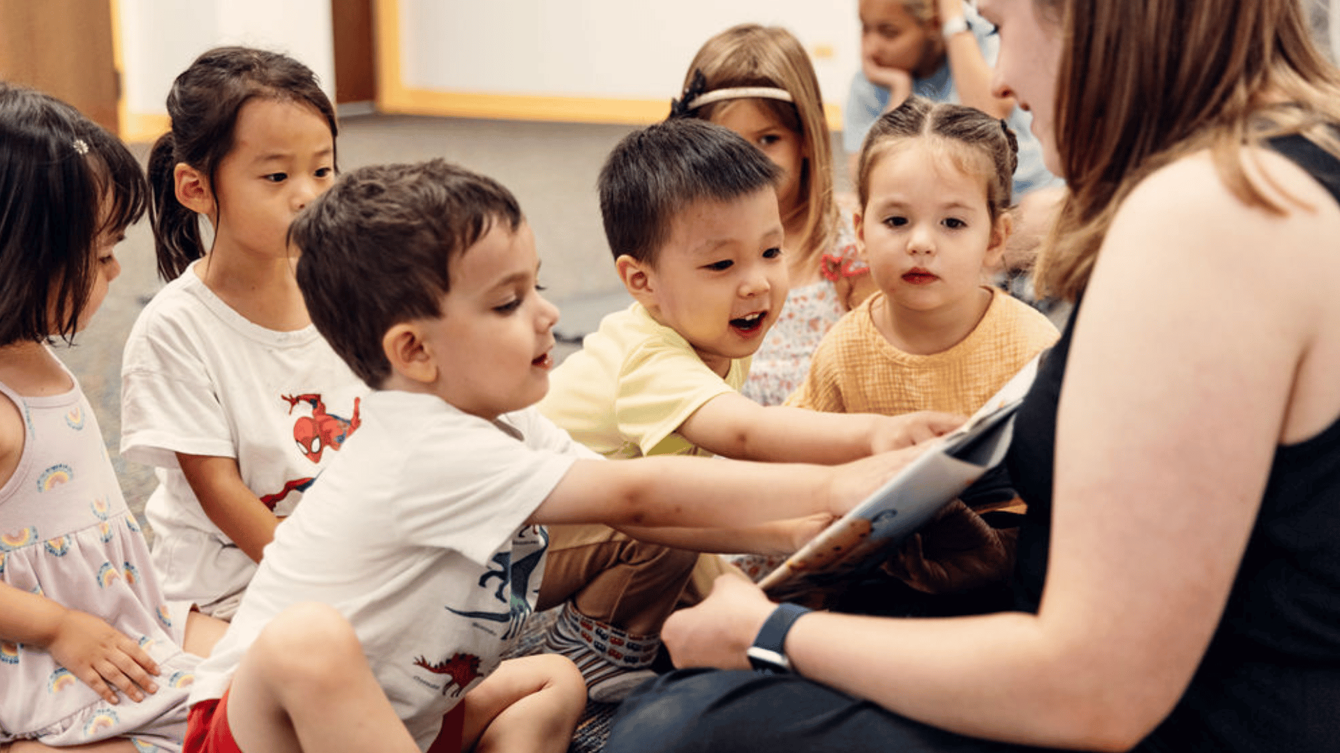 Children point at a book being read to them by a teacher in an Early Childhood class.
