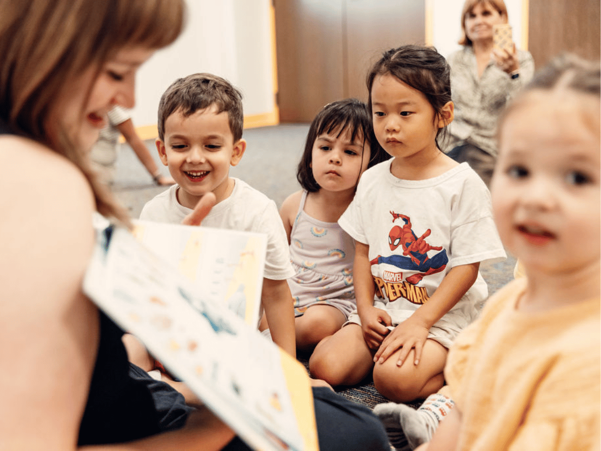 Several children gather around the teacher, reading a book.