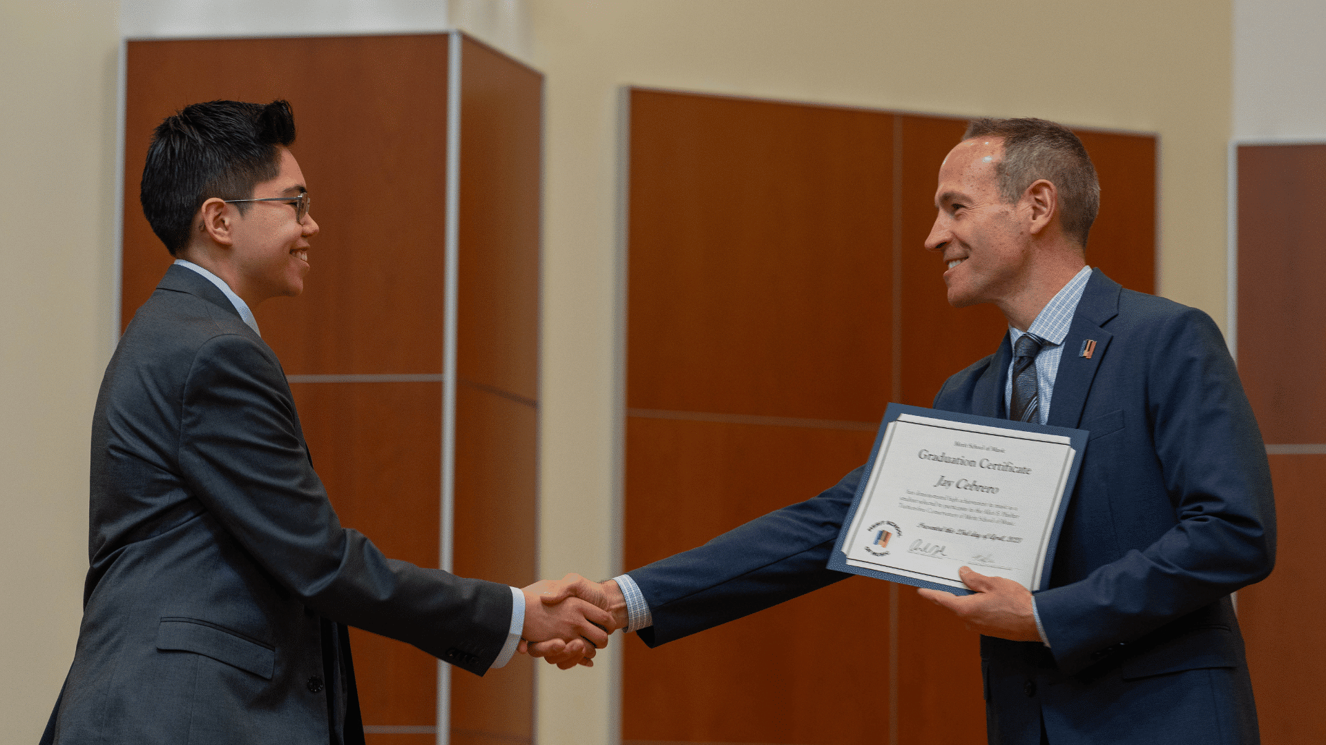 A student shakes hands with Executive Director Charlie Grode, who is holding their diploma.