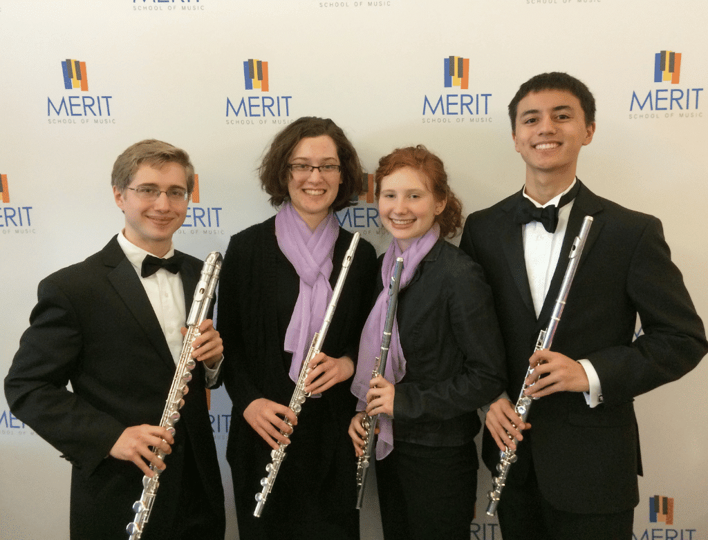 The 2014-2015 Purple Hippopotami pose together in front of a Merit School of Music step and repeat holding their flutes.