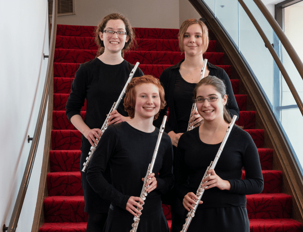 The 2015-2016 Purple Hippopotami pose together holding their flutes on a red staircase.
