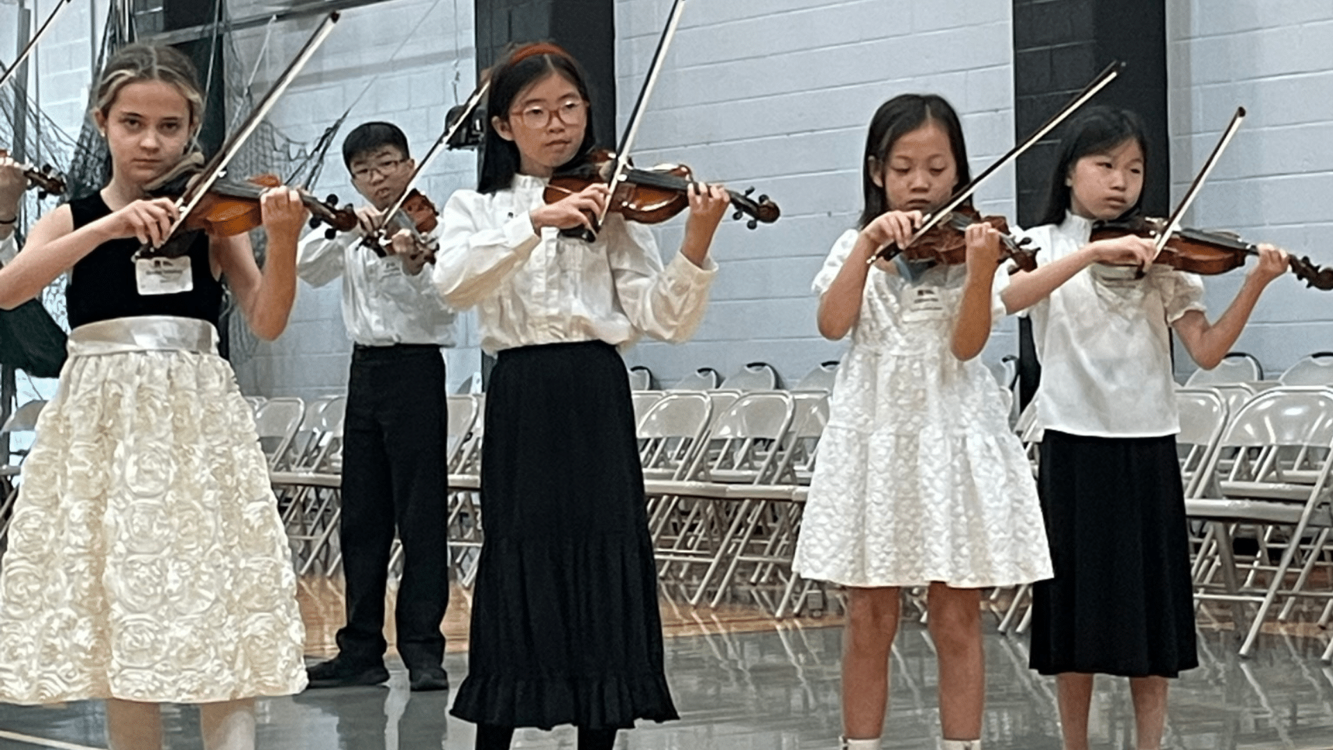 Five young children play violin.
