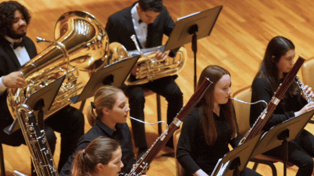 Students in the wind ensemble sit together on stage.