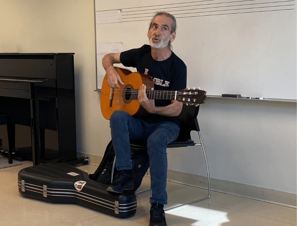 Paco Fonta holding a guitar at the front of a classroom.