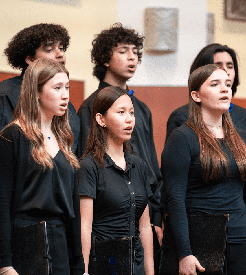 A group of students in black outfits sings in a choir onstage.