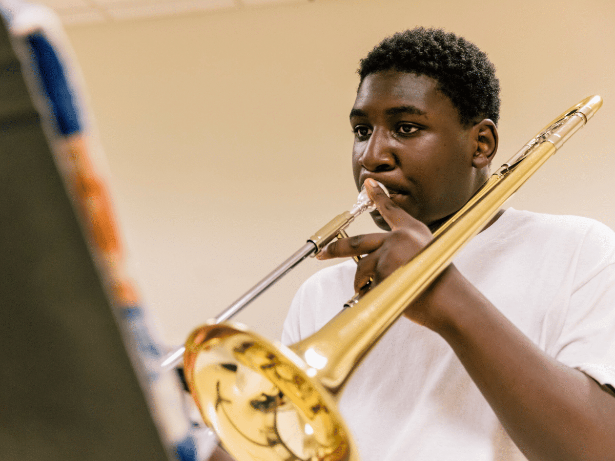 A student playing trombone, looking at music on a music stand.