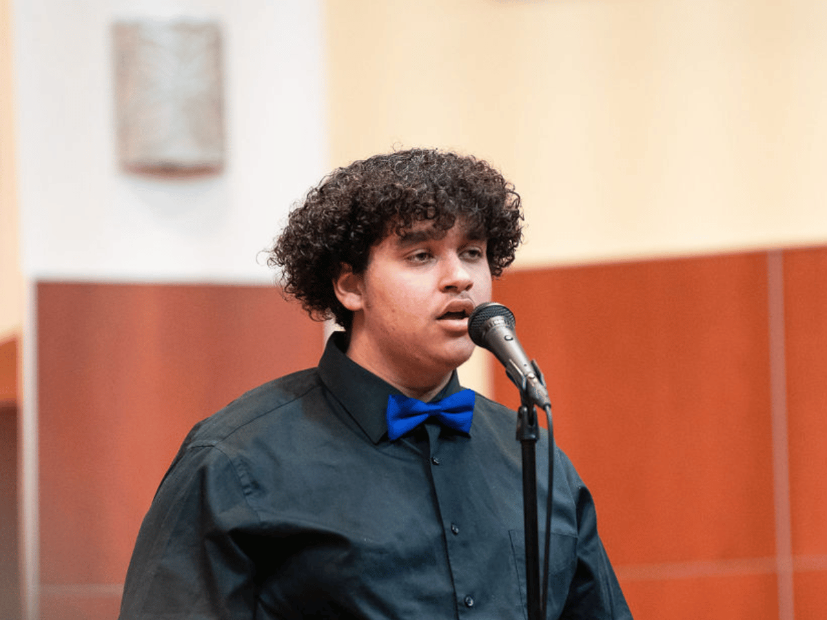 A student sings onstage in front of a microphone.