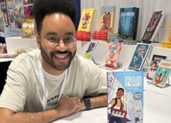 Austin Parmore sits at a table smiling, with his book on the table