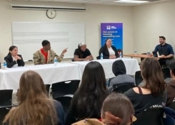 Four alums sit at a panel table with a moderator. The speaker gestures.