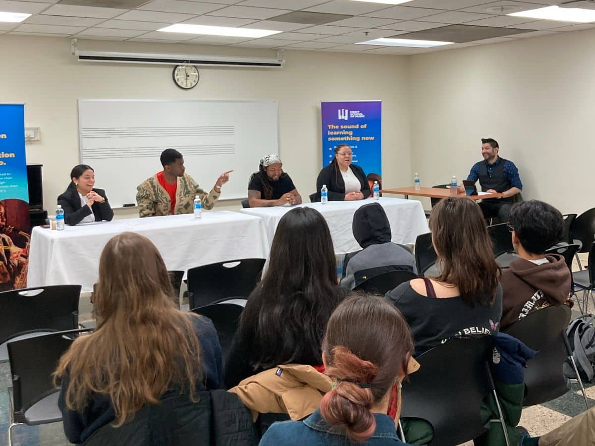 A table of panelists talks in front of a room of students