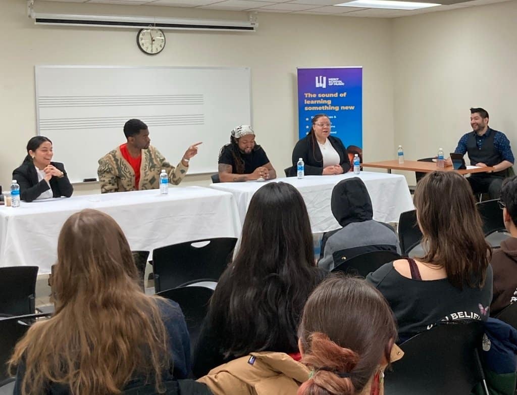 A table of panelists talks in front of a room of students