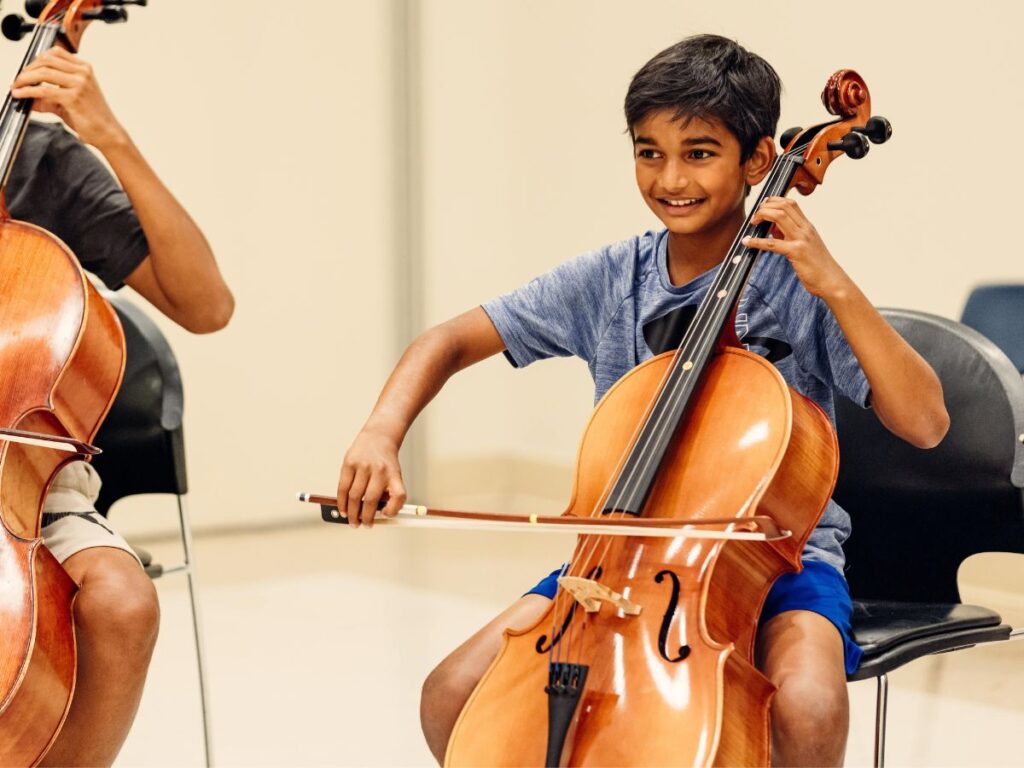 A Suzuki Method student plays the cello and smiles