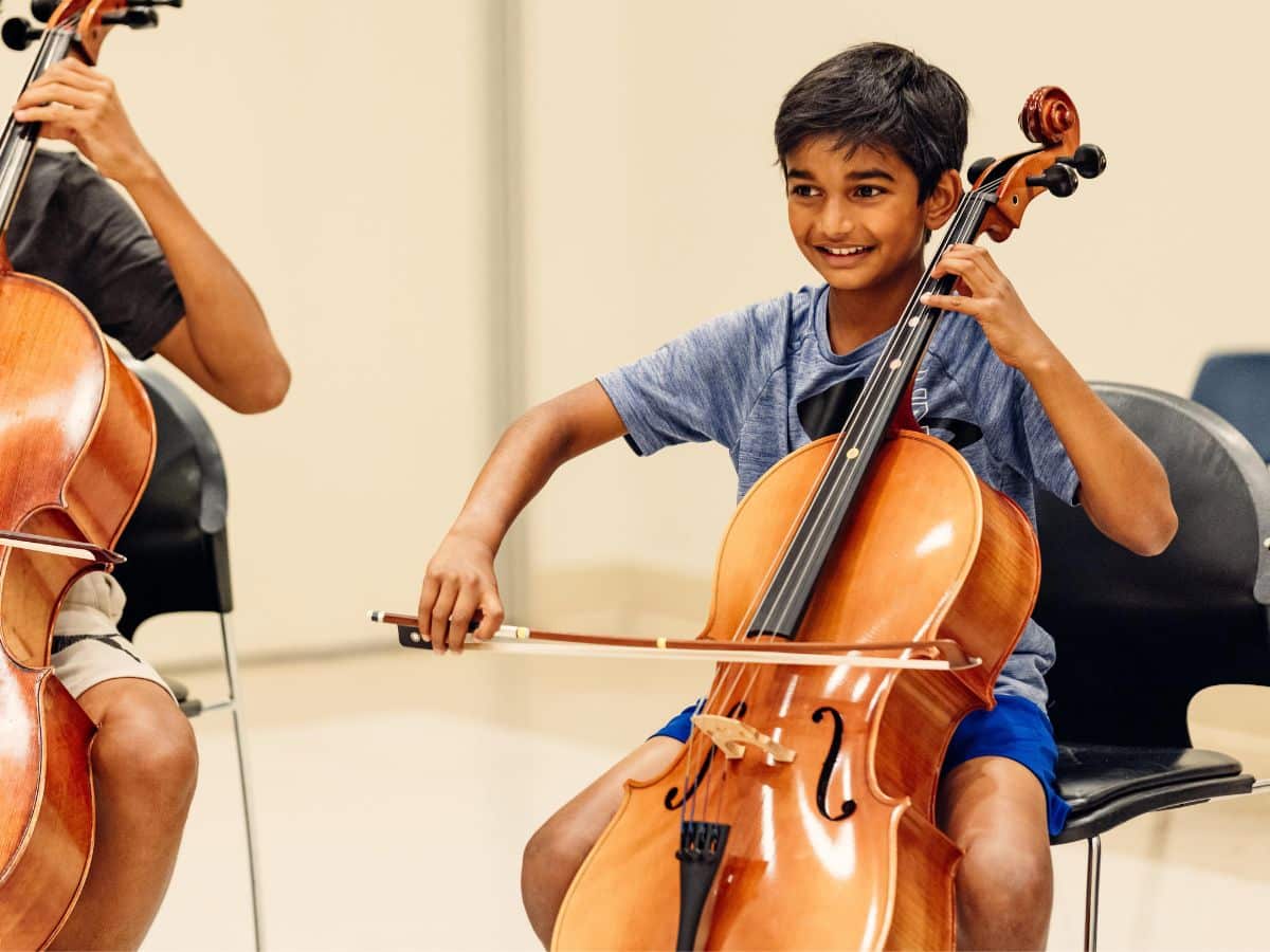 A Suzuki Method student plays the cello and smiles