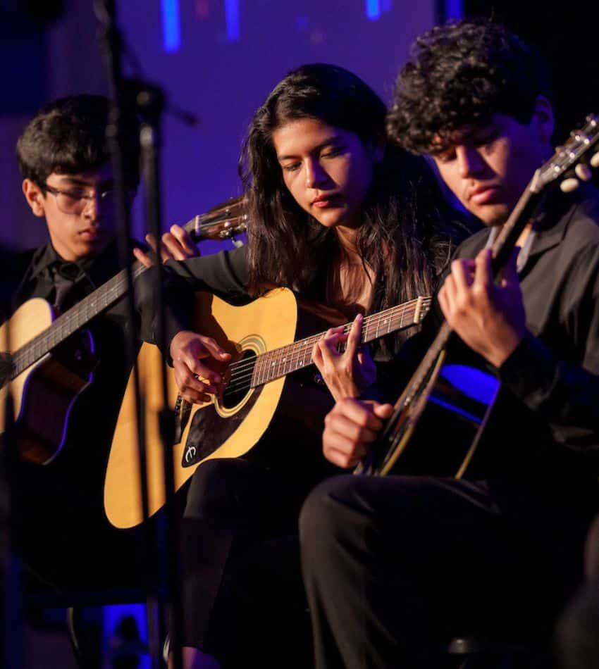 Three students play acoustic guitar onstage