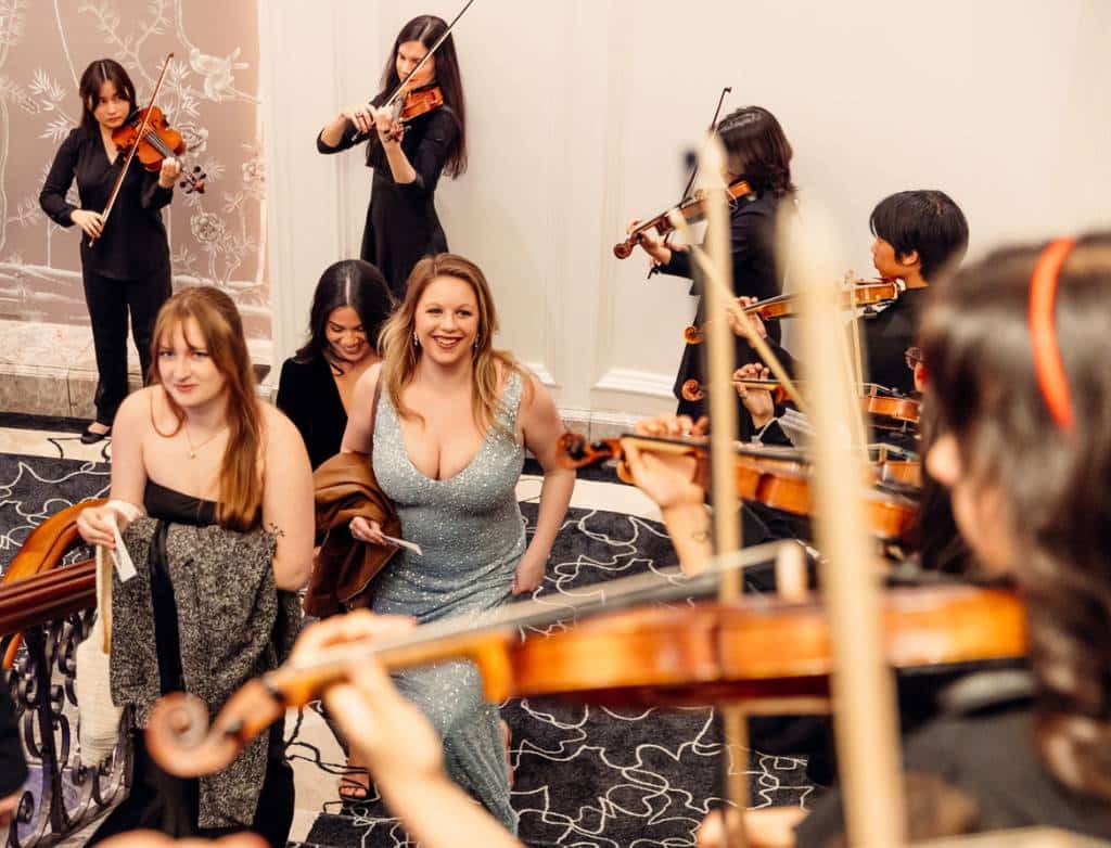 Three guests climb the stairs surrounded by violinists