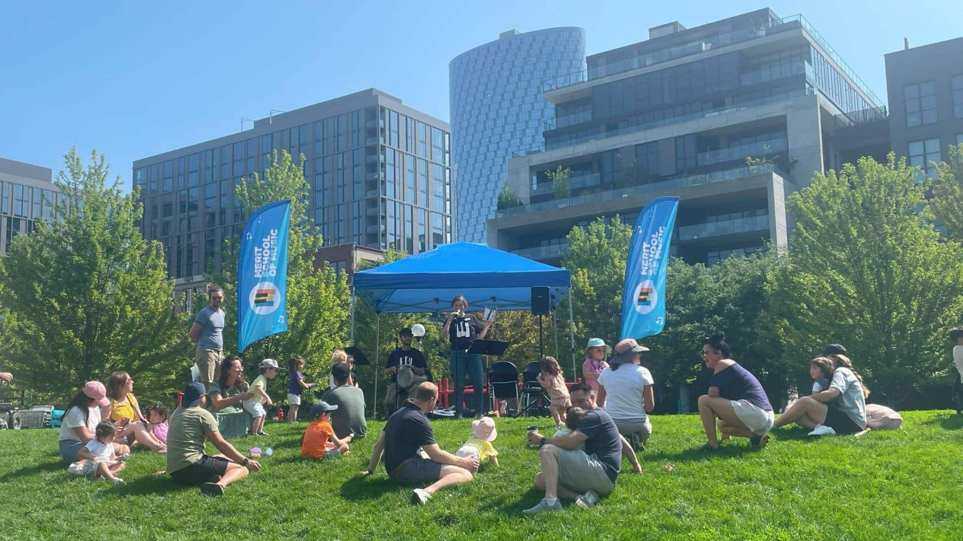 Two performers under a tent, while children and parents sit on the grass and listen