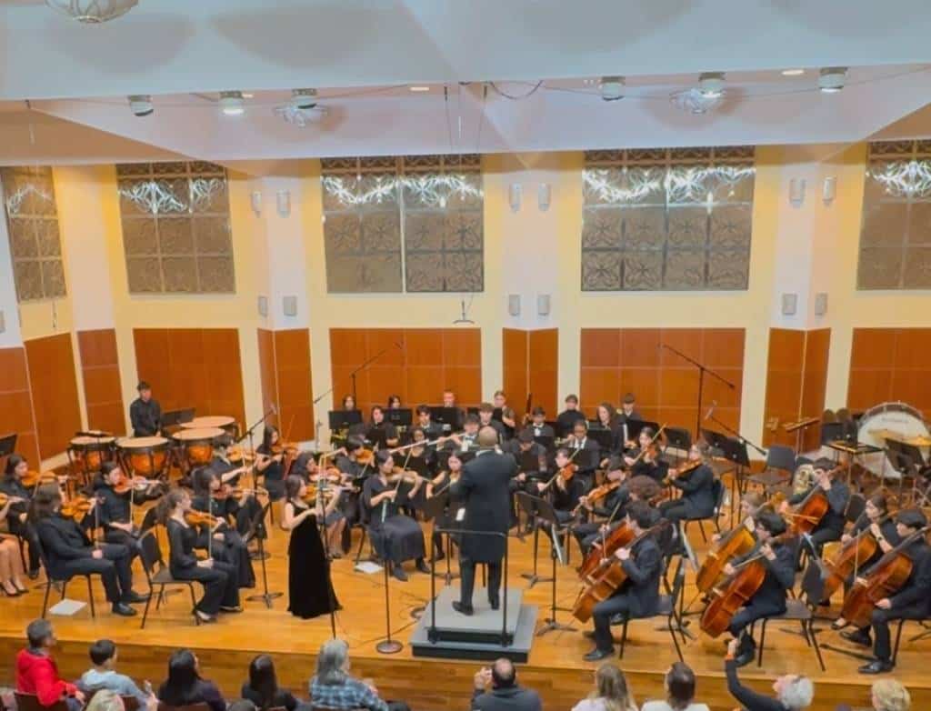 A large orchestra onstage, with a teen violinist solo standing in front