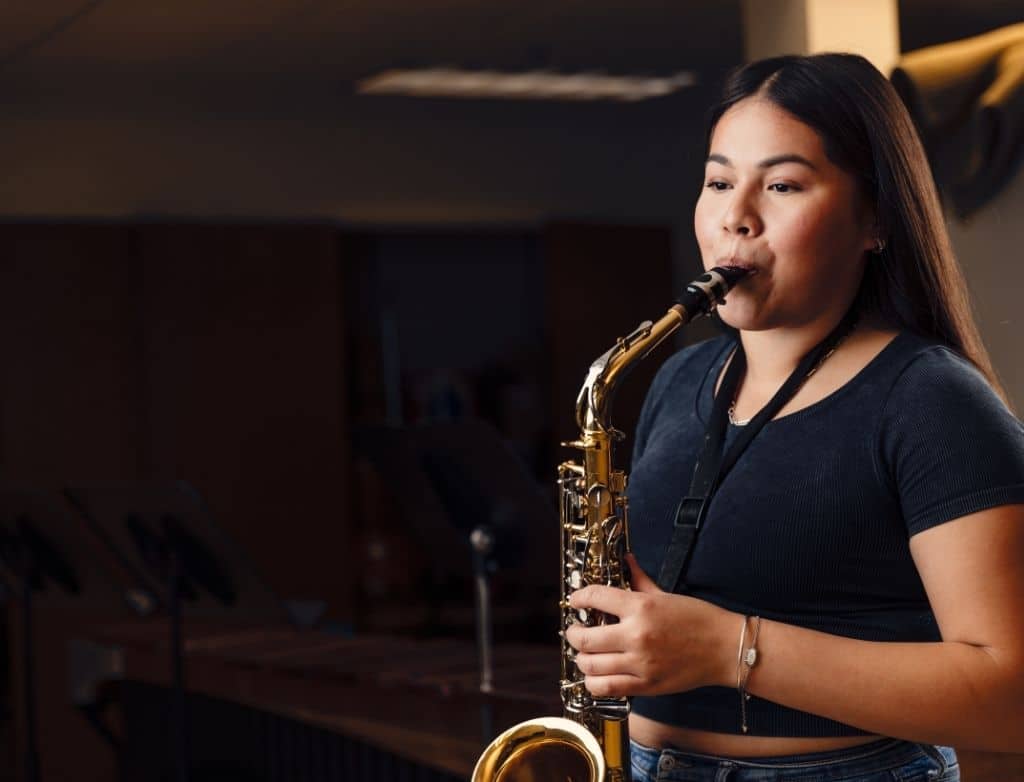 A student plays saxophone in a dark room.