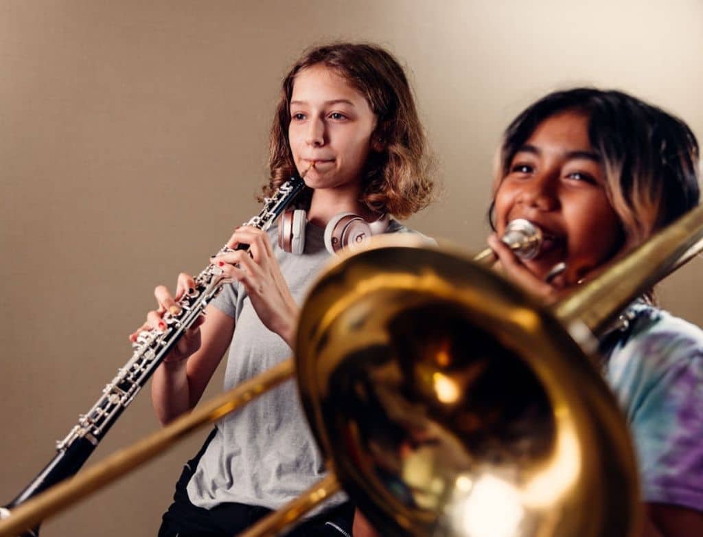 A girl playing oboe beside a girl playing trombone