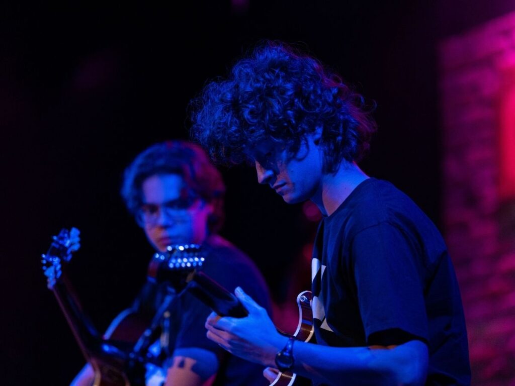 Two Merit students play guitar onstage under blue lights