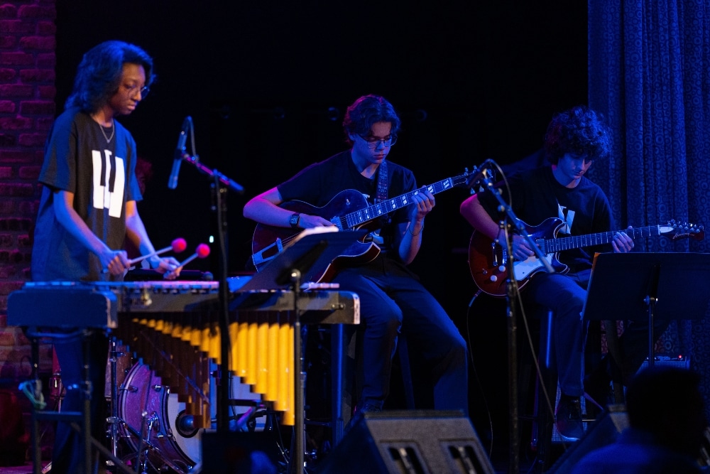 Three students in the Honors Jazz Combo perform onstage, playing vibraphone and guitars.