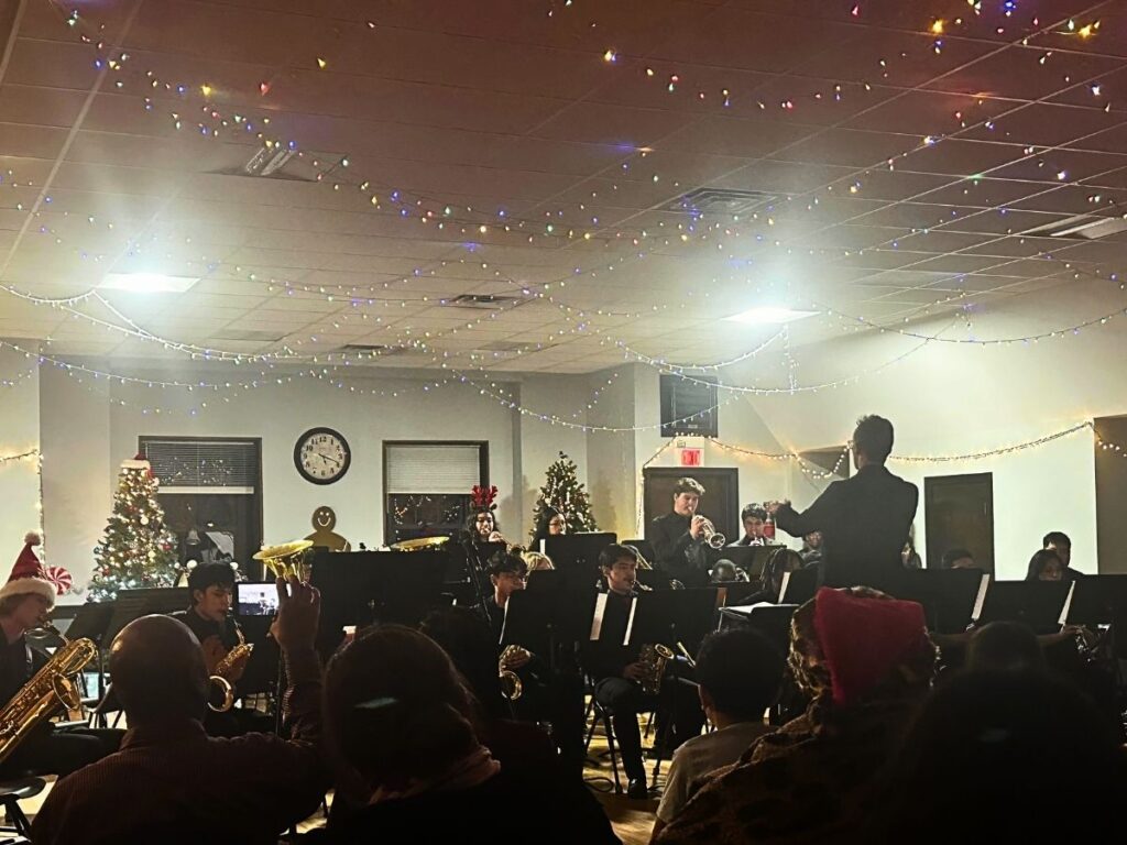Students perform in front of a crowd, with Christmas lights on the ceiling above them.
