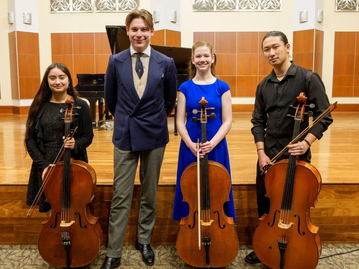 Three students holding cellos pose with Klaus Makela