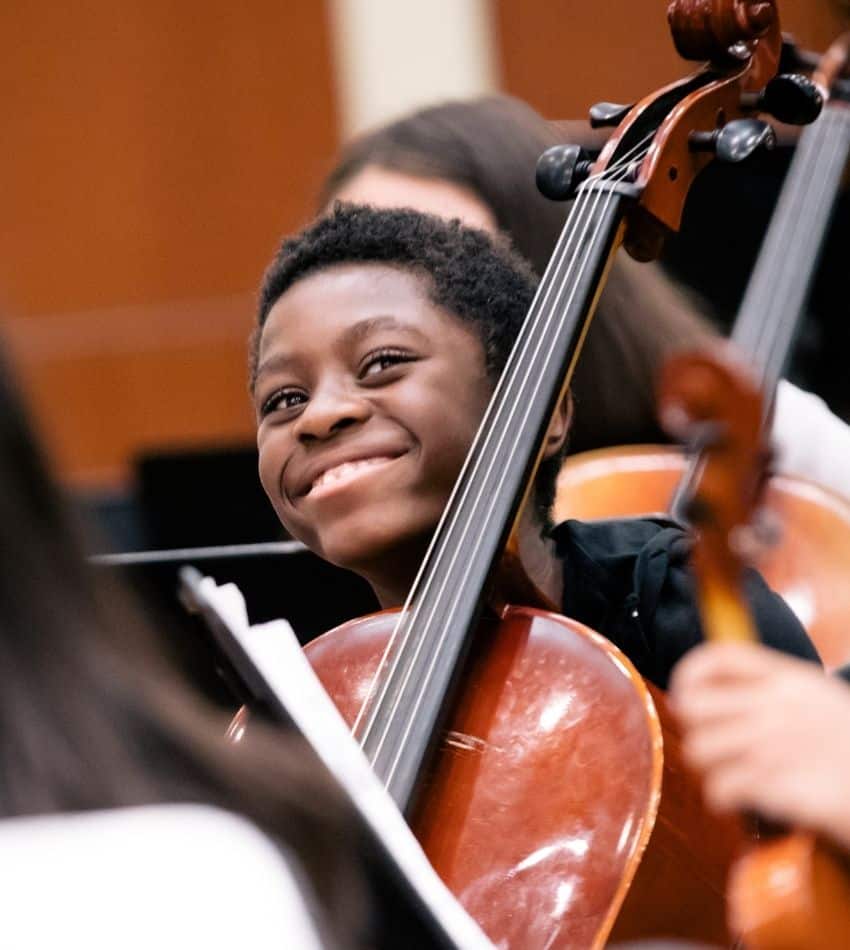 A young boy smiles holding a cello