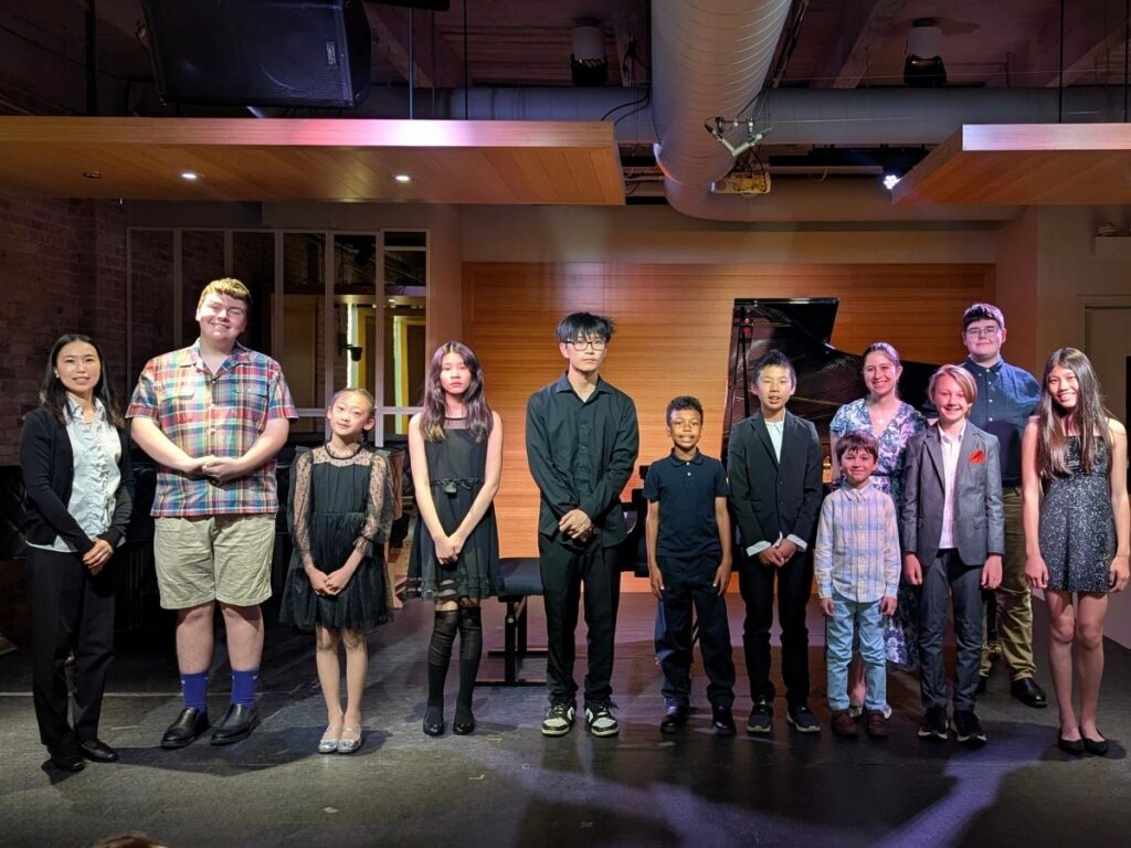 Students stand onstage in a recital hall holding