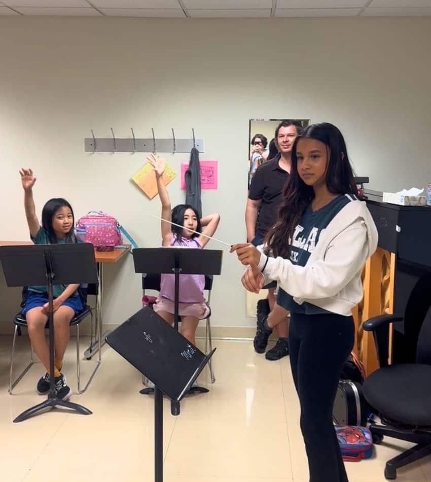 A student conducts while her classmates raise their hands.