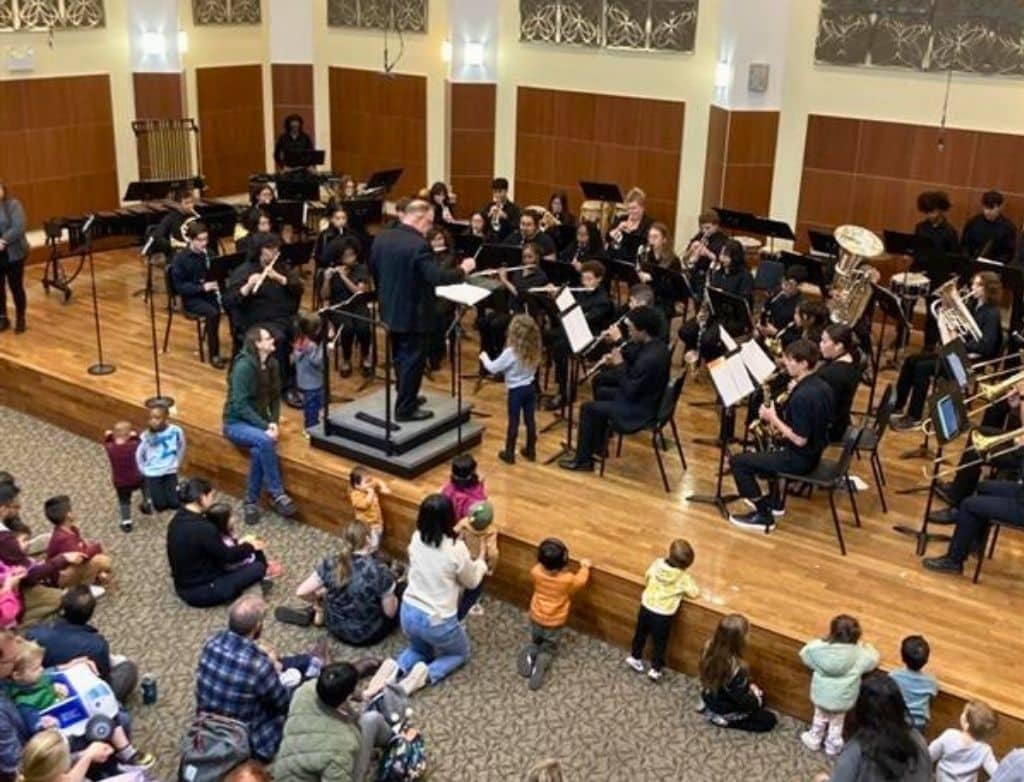 A photo of an orchestra playing while children sit on the floor watching.